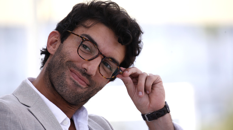 Justin Baldoni smirking, touch glasses rim 