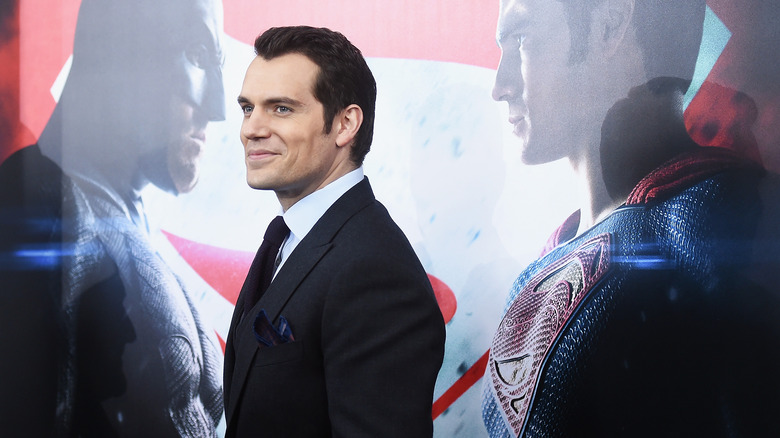 Henry Cavill smirking in front of Superman poster