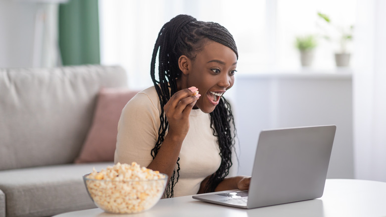 Woman eating popcorn while using her laptop