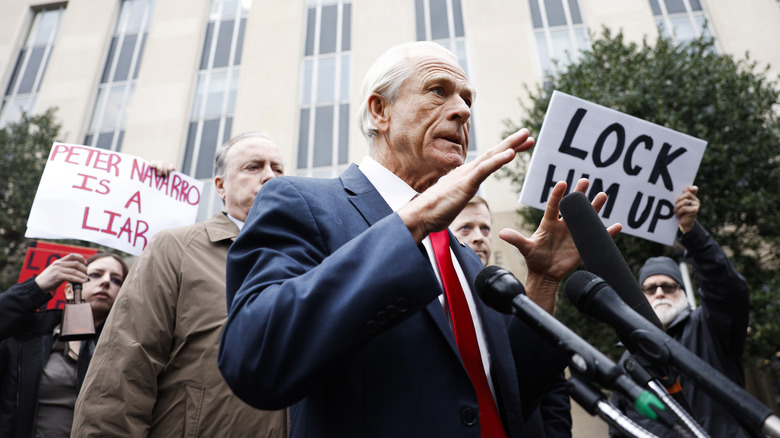 Peter Navarro talking to media on the sidewalk as activists surround him