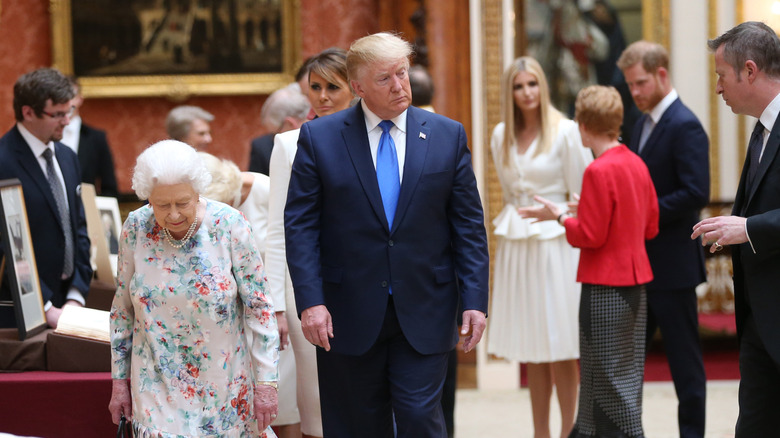 Donald Trump walking in a suit alongside Queen Elizabeth II