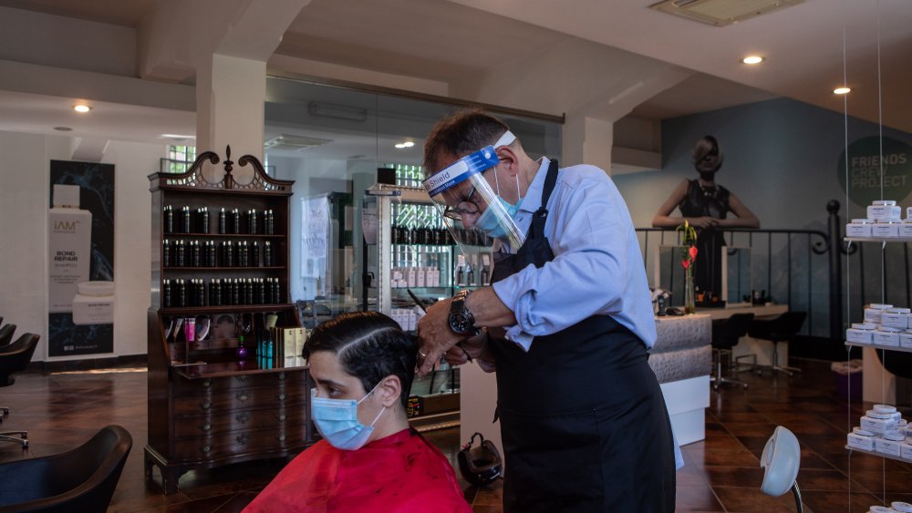 Hairdresser uses a face mask and shield in Italy