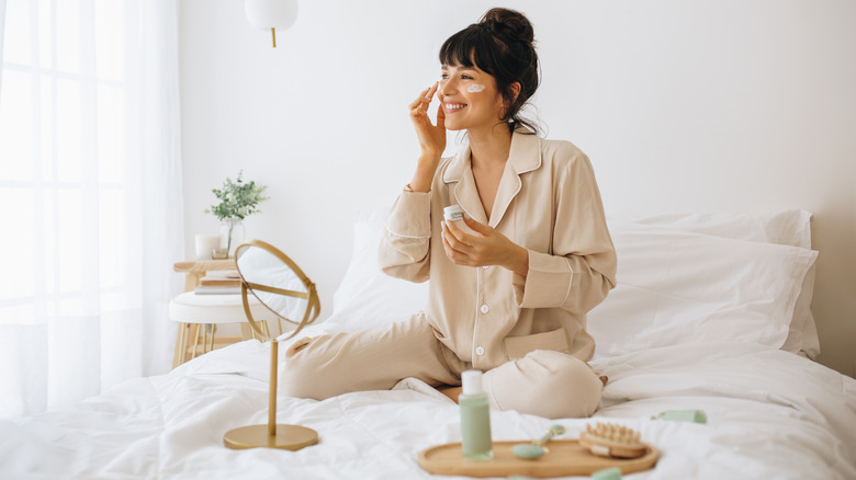 A woman applying skin care in bed