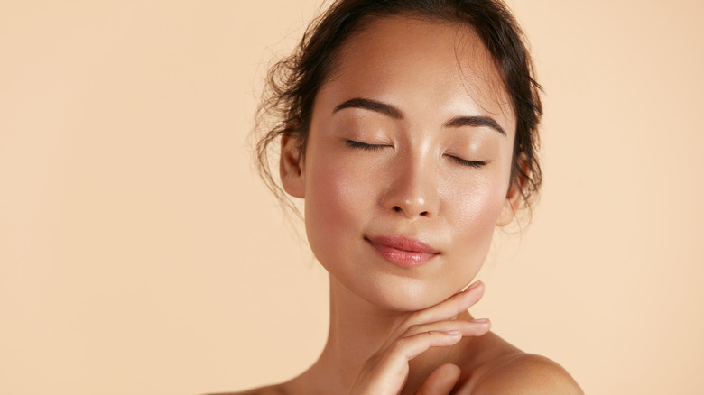 A woman with dewy skin touches her chin.