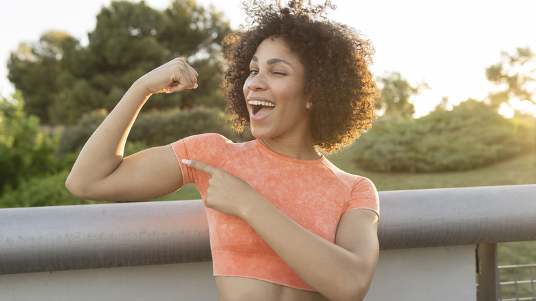 Fit woman smiling while flexing her biceps