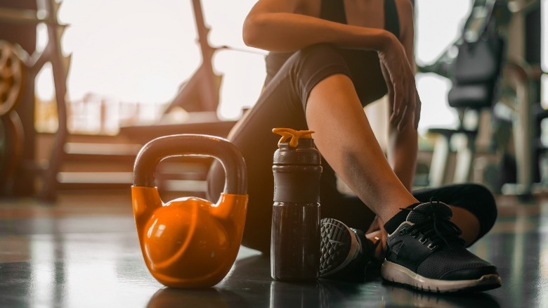 woman sitting on gym floor next to water bottle and kettlebell