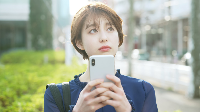 pensive woman holding smartphone