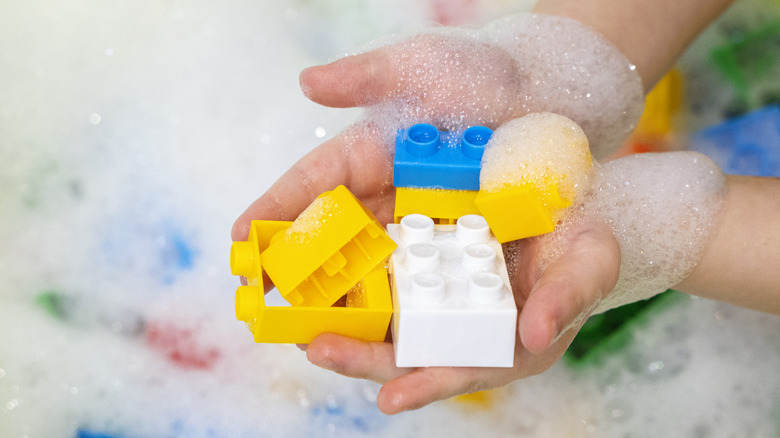 Child foamy Lego blocks in hands with soap foam in background