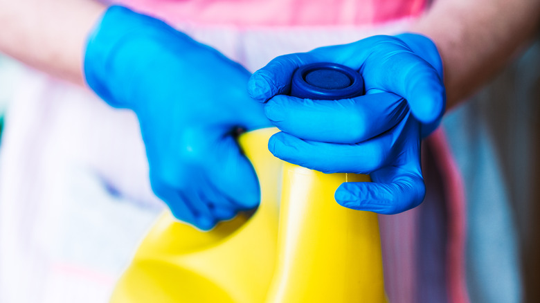 Person opening yellow bleach bottle with blue gloves 