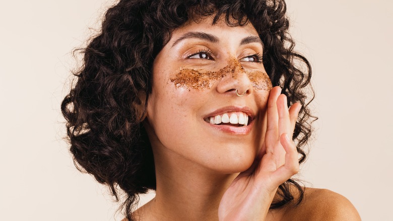 Smiling woman uses exfoliant underneath eyes