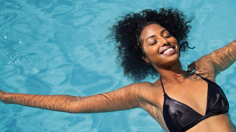 Black woman floating in pool with hair submerged in water