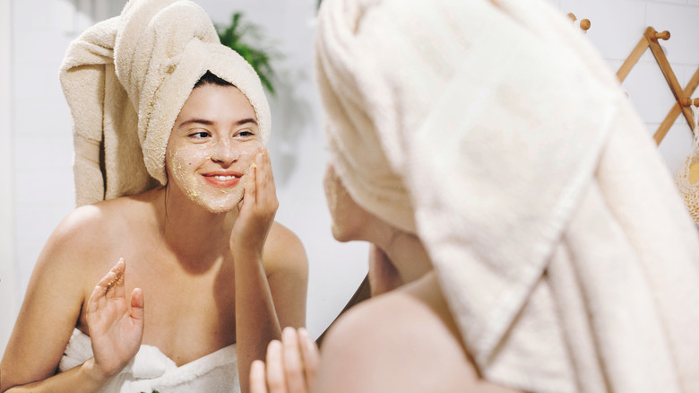 woman exfoliating face while wearing towel