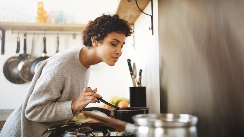 A woman smelling a pot she is stirring 