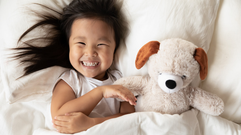 toddler smiling in bed with a stuffy