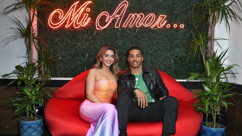 Emeraude Toubia and Rome Flynn on red sofa