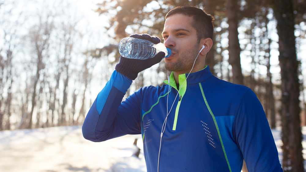 Man drinking a bottle of water in snow-covered woods 