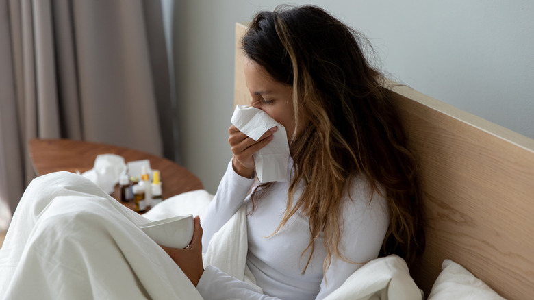 Woman resting in bed blowing nose in a tissue