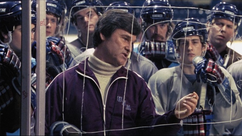 Kurt Russell with other Miracle actors behind hockey rink glass