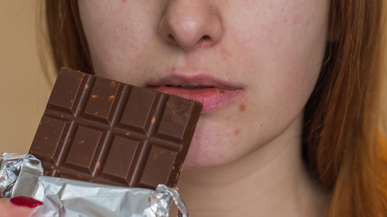 Woman eating chocolate, a potential trigger for acne breakouts 