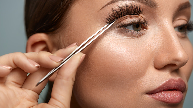 Woman applying fake eyelashes with tweezers