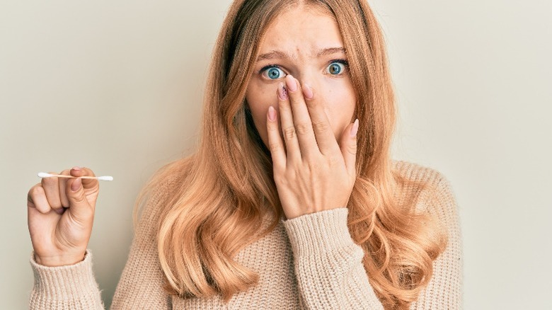 Woman covering mouth and holding Q-tip